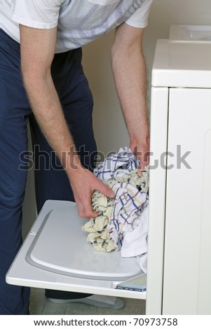 Man loading clothes into dryer dressed in casual clothes.