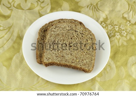 Two crisp whole sprouted grain and legume bread slices on a round white dish above a buttery yellow floral cloth placemat.