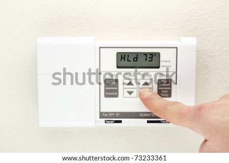 Finger pushing control buttons on heating and cooling digital wall panel display.