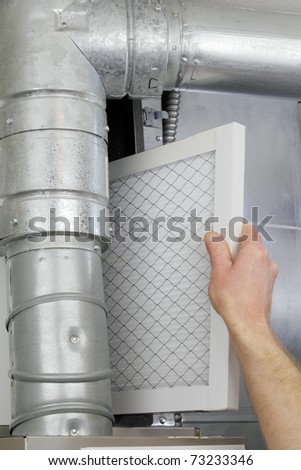 A man\'s arm and hand seen replacing disposable air filter in home central air furnace.