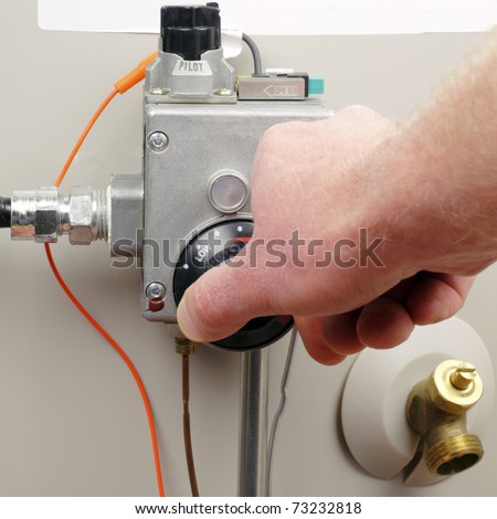 Hand of a man turning down household gas water heater temperature.