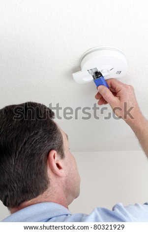 Man carefully replacing 9 volt battery in round white ceiling smoke alarm detector for the safety of his household.