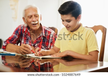 Happy little boy doing school homework with old man at home. Family relationship between grandfather and grandson. Grandpa teaching, male grandchild learning