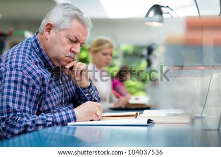 Elderly man studying with a group of young college students in library and taking notes