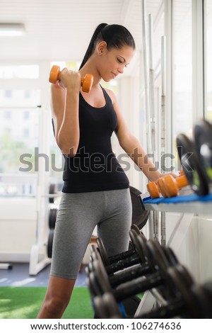 Sports and fun, young female caucasian athlete taking weights from shelf in fitness gym