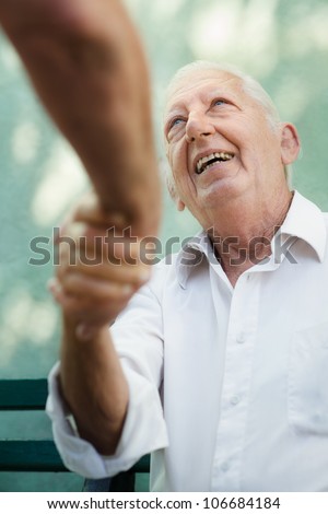 Active retirement, two old male friends talking and shaking hands on bench in public park