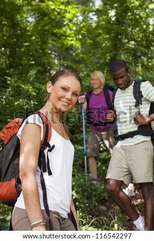 group of man and women during hiking excursion in woods, with woman looking at camera and smiling. Waist up