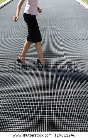 cropped view of mid adult business woman walking on high heels, trying to balance on grating