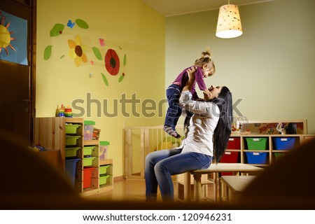 People having fun at school, female educator lifting mid-air child in kindergarten