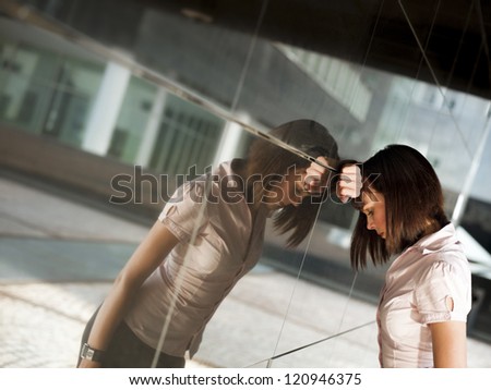 sad caucasian business woman banging her head against a wall out of office building. Reflection on wall