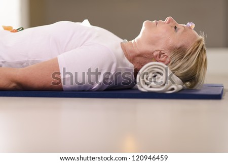 Senior woman relaxing and lying on pad with amethyst, quartz and other crystals on body. Side view, copy space