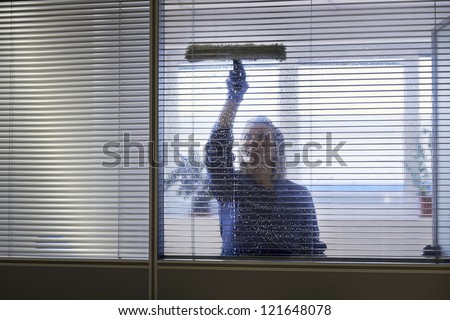 Woman at work, professional female cleaner cleaning and wiping window in office with detergent