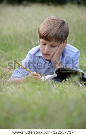 Young people and education, school child doing homework, laying down on grass at park and studying with book. Medium shot, copy space
