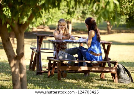 Young women at school, two female friends studying together for college test in park. Full length