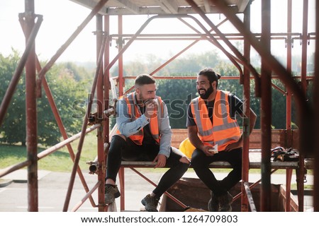 People working in construction site. Men at work in new housing project. Team of happy workers laughing, talking and eating snack during lunch break