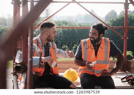 People working in construction site. Men at work in new housing project. Team of happy workers laughing, talking and eating snack during lunch break