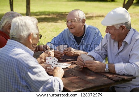Active retirement, old people and seniors free time, group of four elderly men having fun and playing cards game at park. Waist up