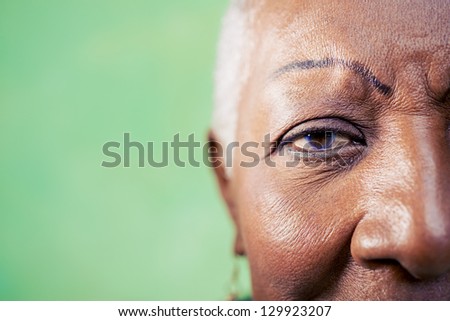 Old black woman portrait, close-up of eye and face on green background. Copy space