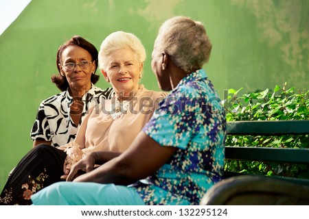 Active retired elderly women and free time, group of happy senior african american and caucasian female friends talking and sitting on bench in park
