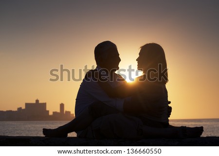 Elderly couple in love, honeymoon with old man and woman kissing near the sea at sunset in La Habana, Cuba. Silhouette of couple and skyline of the city