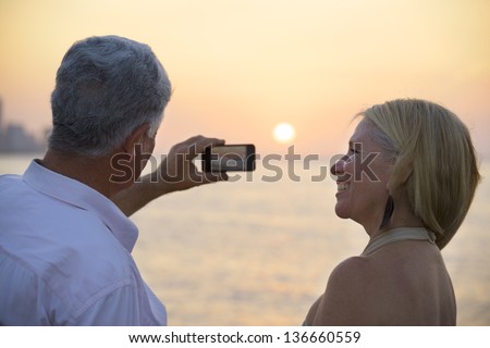Travel and active elderly man and woman, couple of tourists looking at sea and taking picture with smartphone