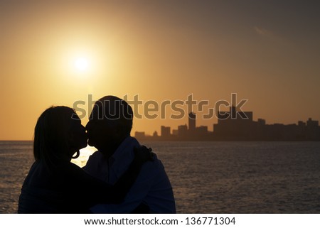 Elderly couple in love, honeymoon with old man and woman kissing near the sea at sunset in La Habana, Cuba. Silhouette of couple and skyline of the city
