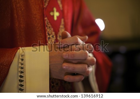 Catholic priest on altar praying with hands joined during mass service in church