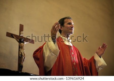 Catholic priest on altar praying with open arms during mass service in church
