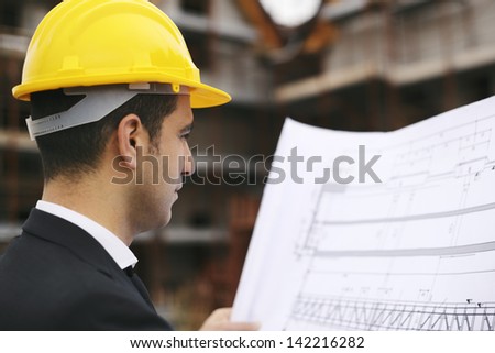 Young man working as engineer in new apartment buildings, looking at building plan in construction site
