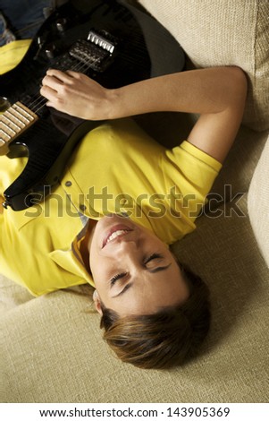 beautiful mid adult woman playing electric guitar at home, laying on sofa