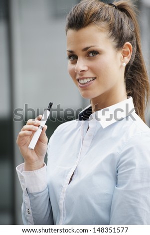 portrait of young female smoker smoking e-cigarette outdoor office building and looking at camera