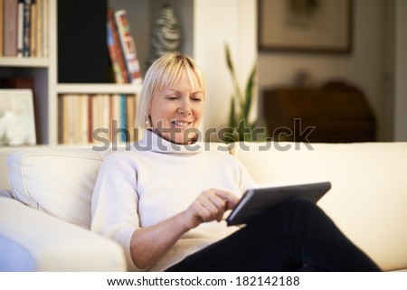 portrait of beautiful old woman using tablet pc and smiling, sitting on sofa at home