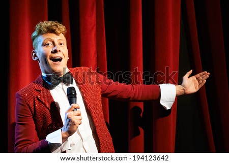 Arts and entertainment in theatre with funny man working as anchorman, standing against red curtains with microphone