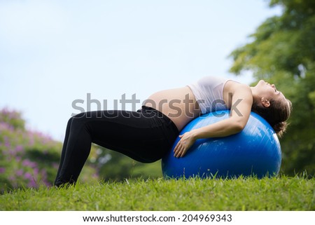 Portrait of white beautiful pregnant woman doing fitness exercise in park working out abs on fitness ball. Copy space