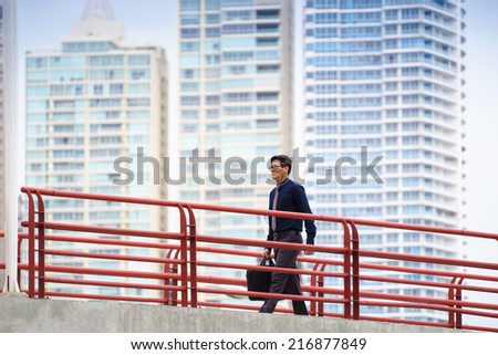 Portrait of chinese businessman walking on bridge in Panama, commuting to work. Skyscrapers in background
