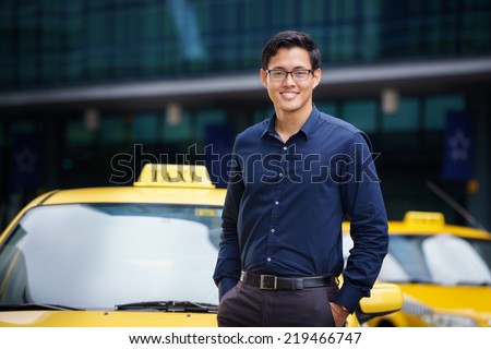 Portrait of happy chinese taxi driver leaning on yellow car with arms crossed, smiling and looking at camera