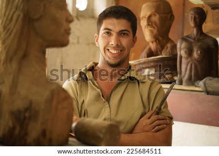 Portrait of man working, young student in art class, learning crafts profession, working with wooden statue and looking at camera