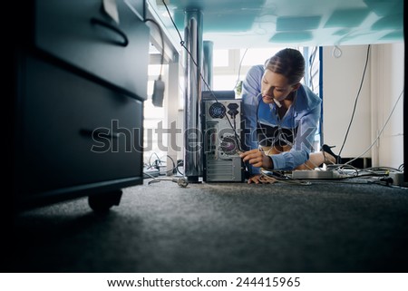 Female assistant working in office, plugging cables to computer and electronic equipment, messing around with wires. Copy space