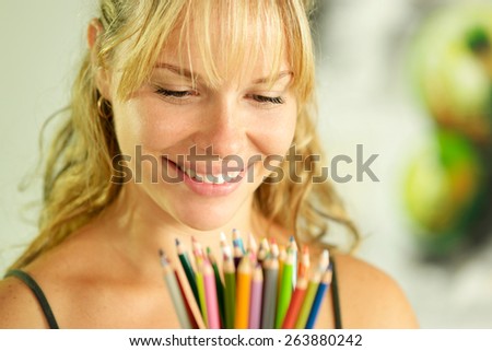 Portrait of young woman holding bunch of colorful pencils at camera and smiling