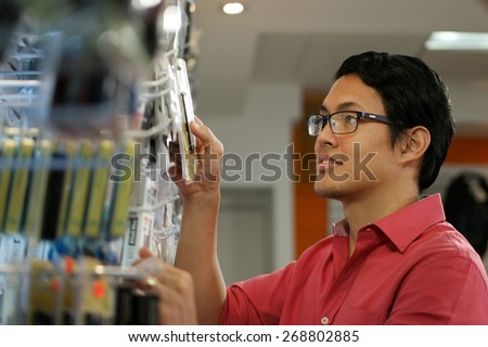 Chinese sales clerk working in computer store, arranging and ordering cables and usb flash memory drives on shelf