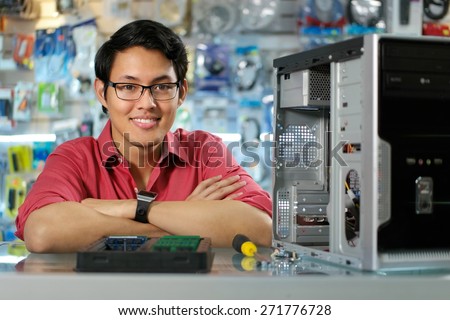 Young asian shop owner working in computer store, repairing computer and adding ram to pc. Portrait of man smiling at camera