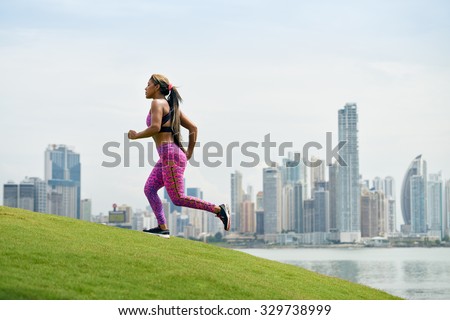Young african american woman running and exercising early morning in the city. She runs on a small hill against the skyline