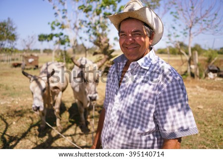Farming and cultivations in Latin America. Portrait of middle aged hispanic farmer sitting proud in his tractor at sunset, holding the volante. He looks at the camera and smiles happy.