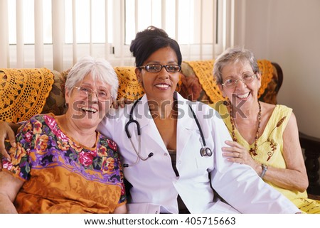 Old people in geriatric hospice: Elderly man and woman hugging an african american doctor, showing a friendly relationship between personnel and patients.