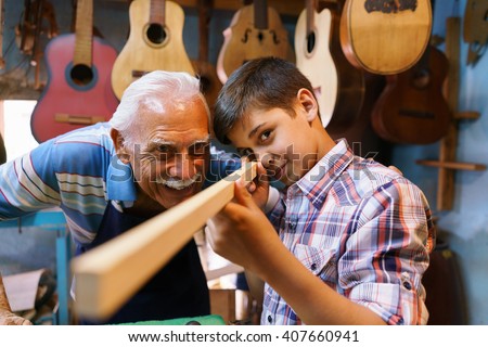 Small family business and traditions: old grandpa with grandson in lute maker shop. The senior artisan teaches to the boy how to chisel wood to make a music instrument.