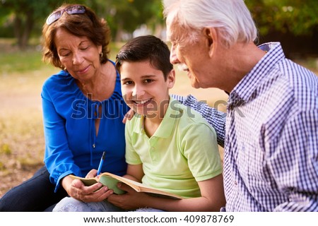 Grandparents educating grandson: Senior woman and old man spending time with their grandchild in park. The old people help the preteen boy doing his school homework. The kid looks at camera