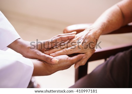Old people in geriatric hospice: Aged patient receives the visit of a female black doctor. They shake their hands and talk in the hospital.
