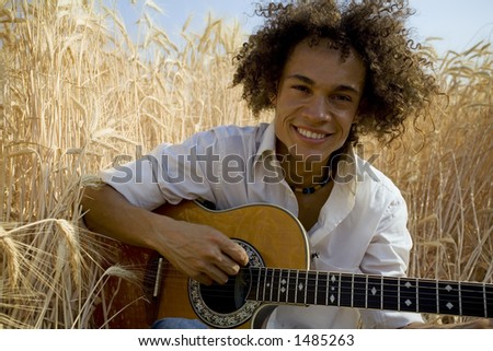 cool guy sitting in a cornfield playing guitar