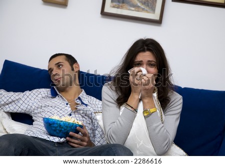 young couple watching a romantic movie on tv. The guy is quite bored....