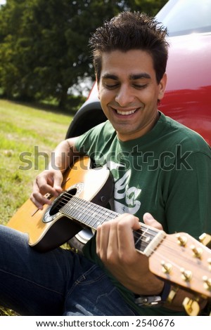 cool guy playing guitar besides his car